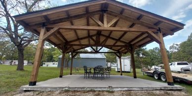 Wooden pavilion with a metal roof and outdoor seating set on concrete.
