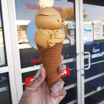 Gluten-free waffle cone with two scoops of ice cream held in front of the entrance of Walia Creamery