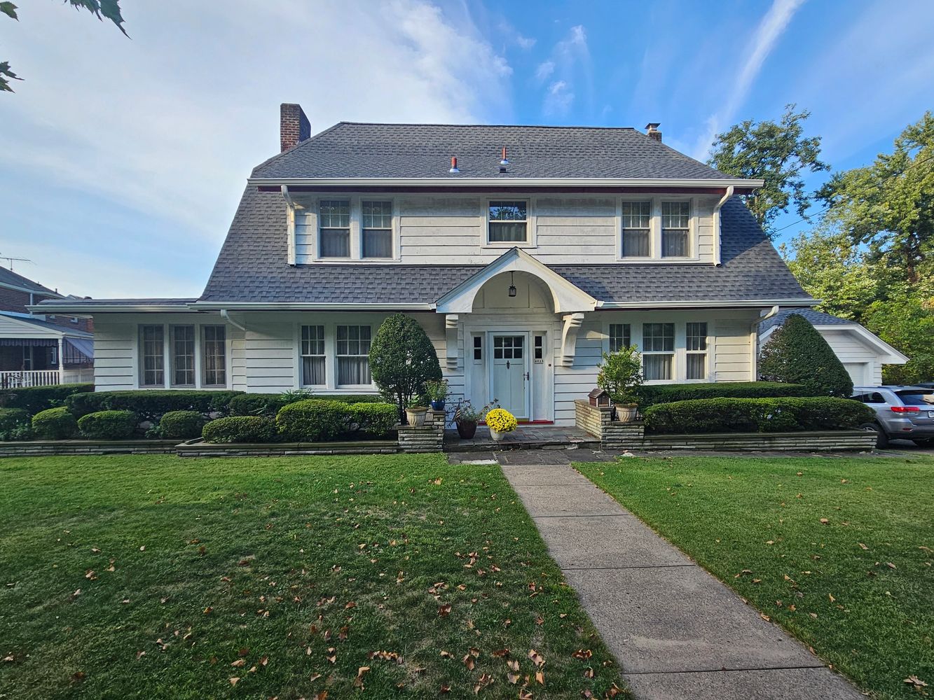 Classic two-story white house with manicured bushes and a stone pathway.