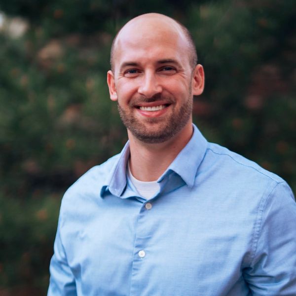 Smiling bald man in blue shirt outdoors.