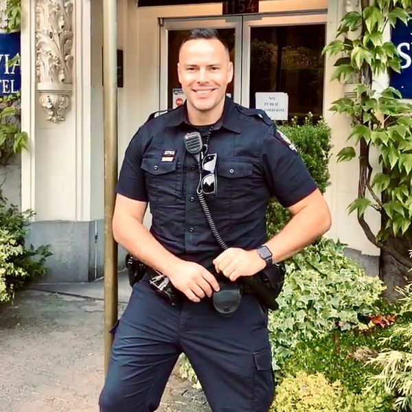 A smiling police officer stands in front of The Sylvia Hotel entrance.