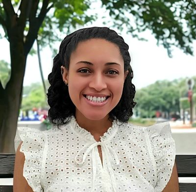 Smiling woman in a white eyelet blouse sitting outdoors on a bench.