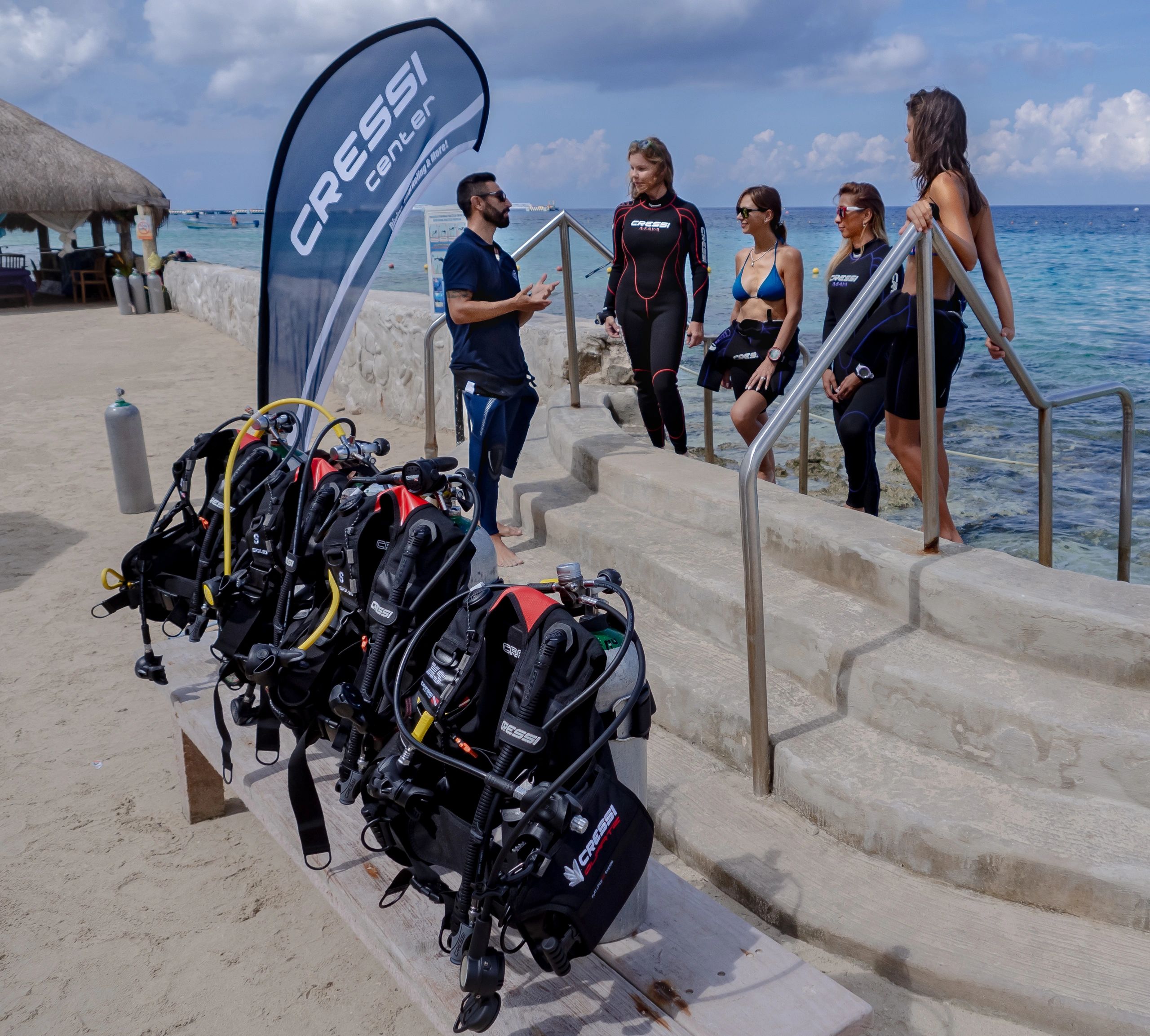 Group receiving scuba diving instructions by the sea at a Cressi center.