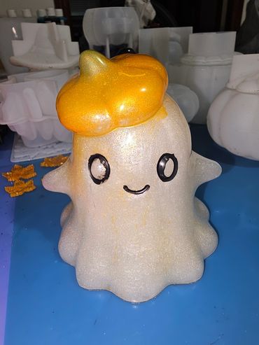 A cute ghost figurine with a golden pumpkin hat on a blue surface.