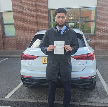 Young man proudly holding a driving test pass certificate in front of a white car.