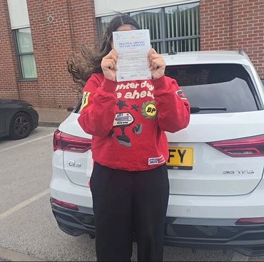 Person proudly holding a driving test pass certificate in front of a white Audi Q3.