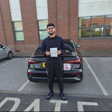 Young man proudly holding a driving certificate in front of a black car with an 'L' plate.