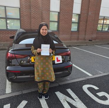 Woman proudly holding a driving test pass certificate in front of a black car with L plates. Female patient calm driving instructor Sheldon Birmingham