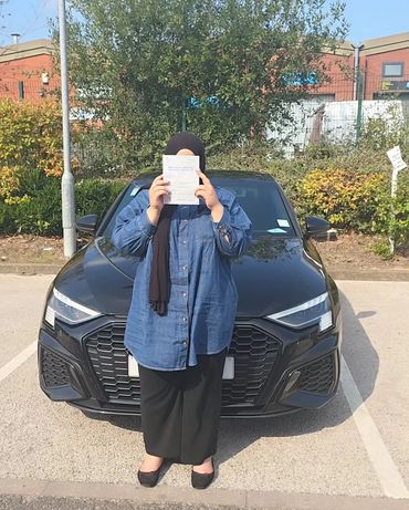 Person in front of a black car holding a document covering their face.