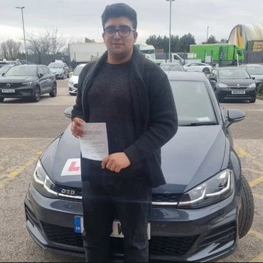 Young man standing in front of a car holding a document, likely a driving test pass certificate.