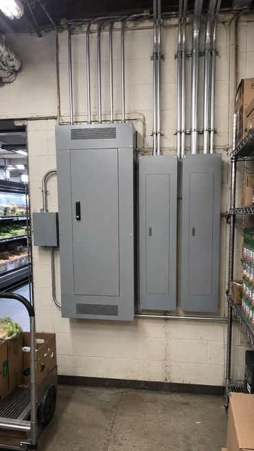 Upgraded commercial electrical panels and conduit in the back stockroom of a small grocery store.