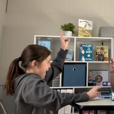 Girl excitedly pointing in a classroom setting.