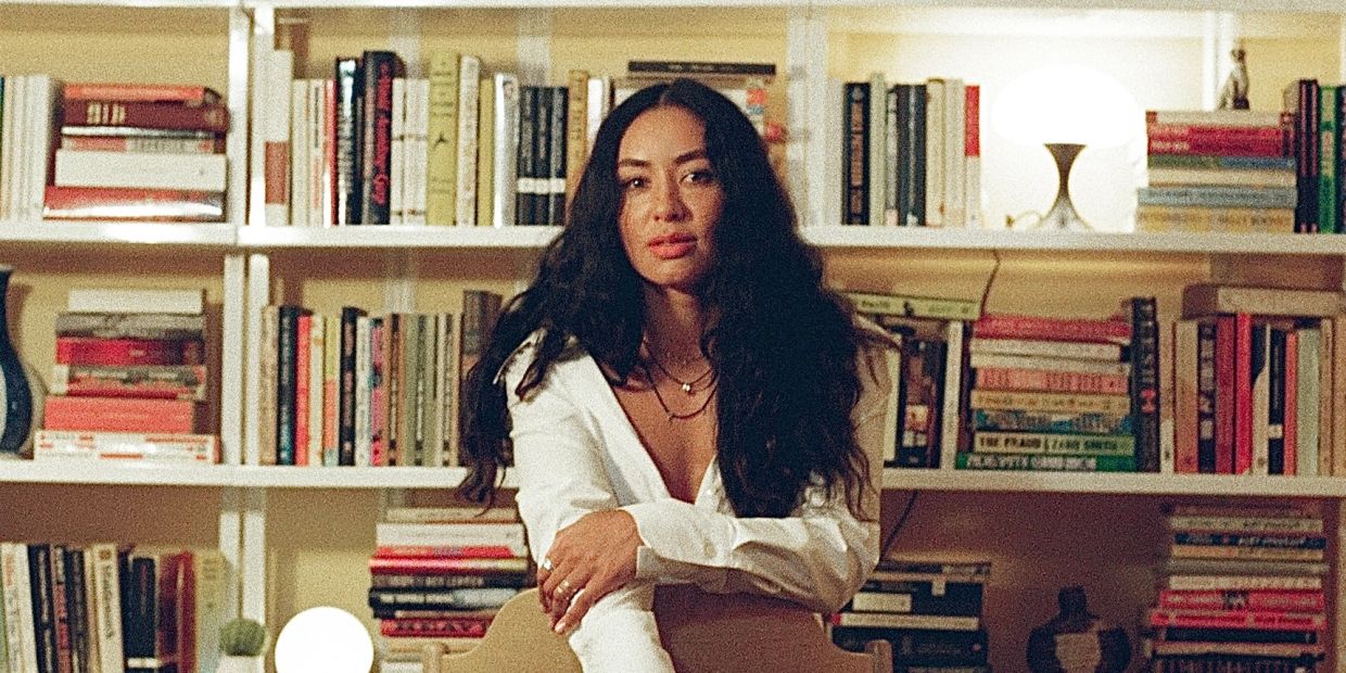 Woman with long hair sitting in front of a bookshelf.
