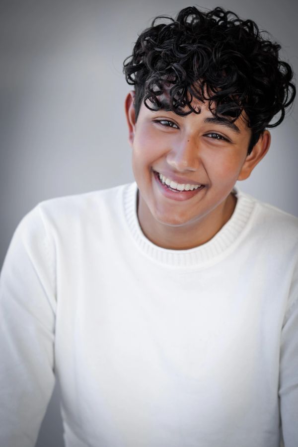 Smiling young person with curly hair in white sweater.