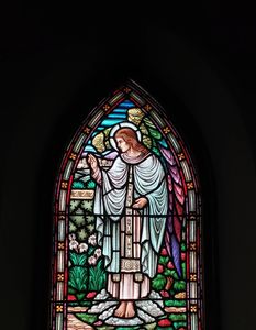 Stained glass window depicting a robed angel with flowers and a dove.