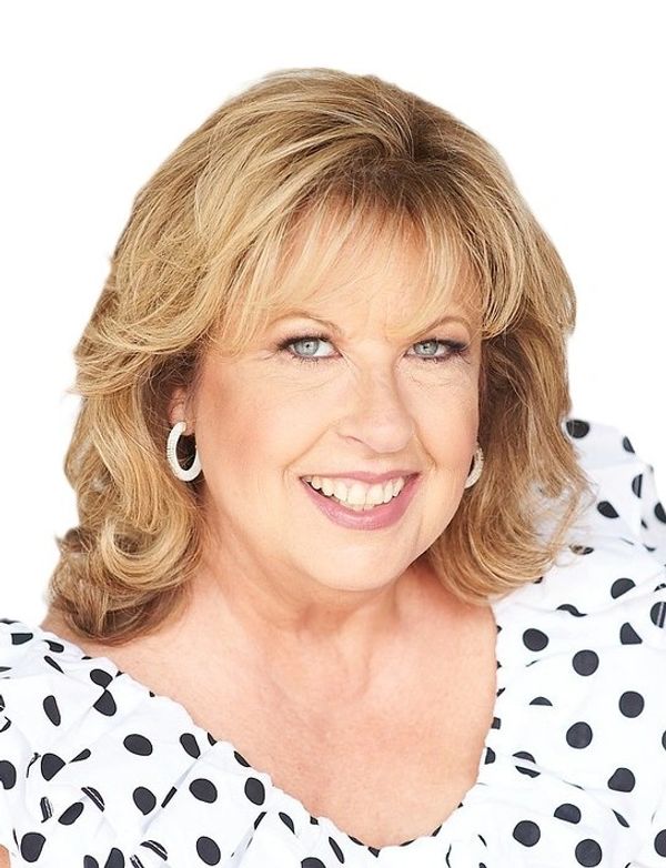 Smiling woman with blonde hair wearing polka dot top and hoop earrings.