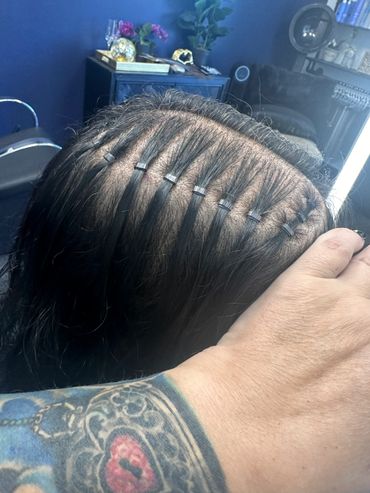 Close-up of hair extensions being installed with small metal beads.