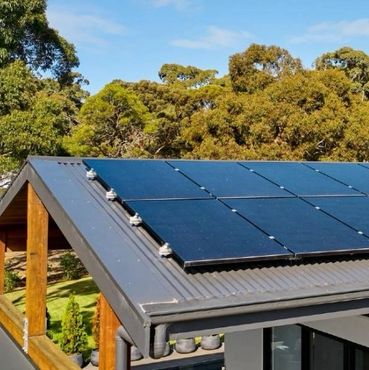Solar panels installed on a modern house roof surrounded by trees.