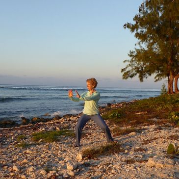 Christine Bhe, certified Tai Chi and Qigong instructor on a rocky beach with blue sky and trees