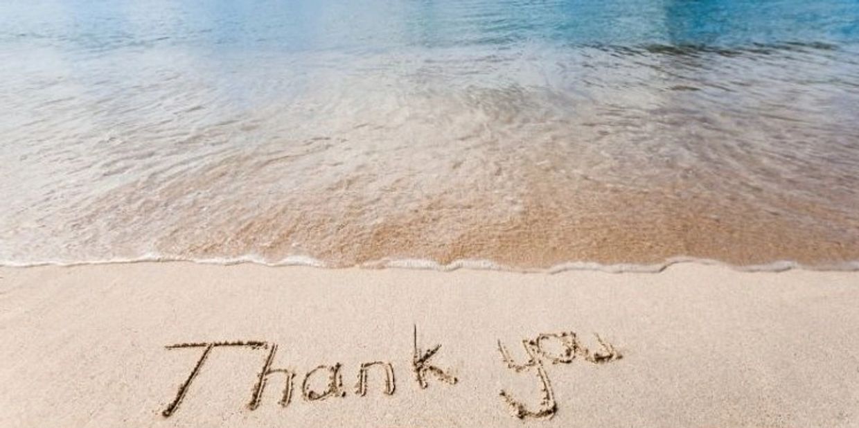 "Thank you" written in sand near the ocean water.