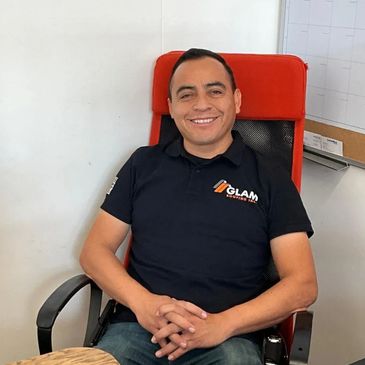 Smiling man seated in office chair wearing a black polo with a logo.