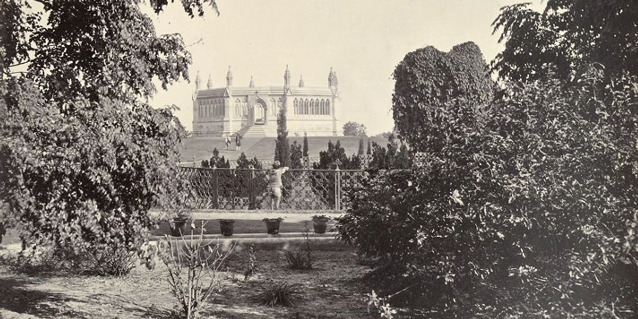 A child looks over a decorative fence towards a grand historic building in a garden setting.