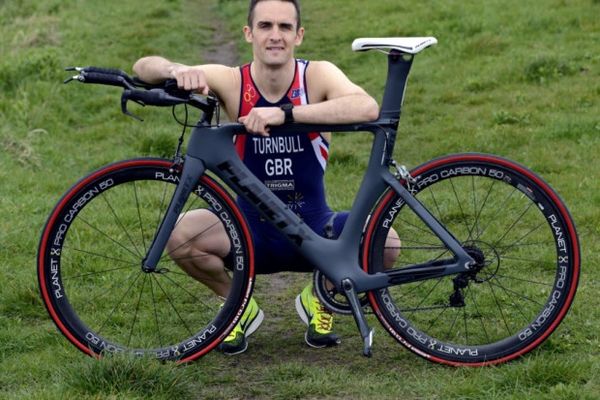 Athlete posing with a sleek black and red racing bike on grass.