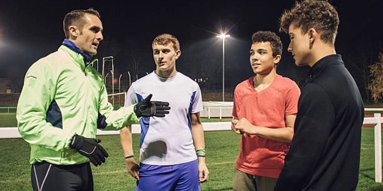 Coach giving instructions to young athletes on a sports field at night.