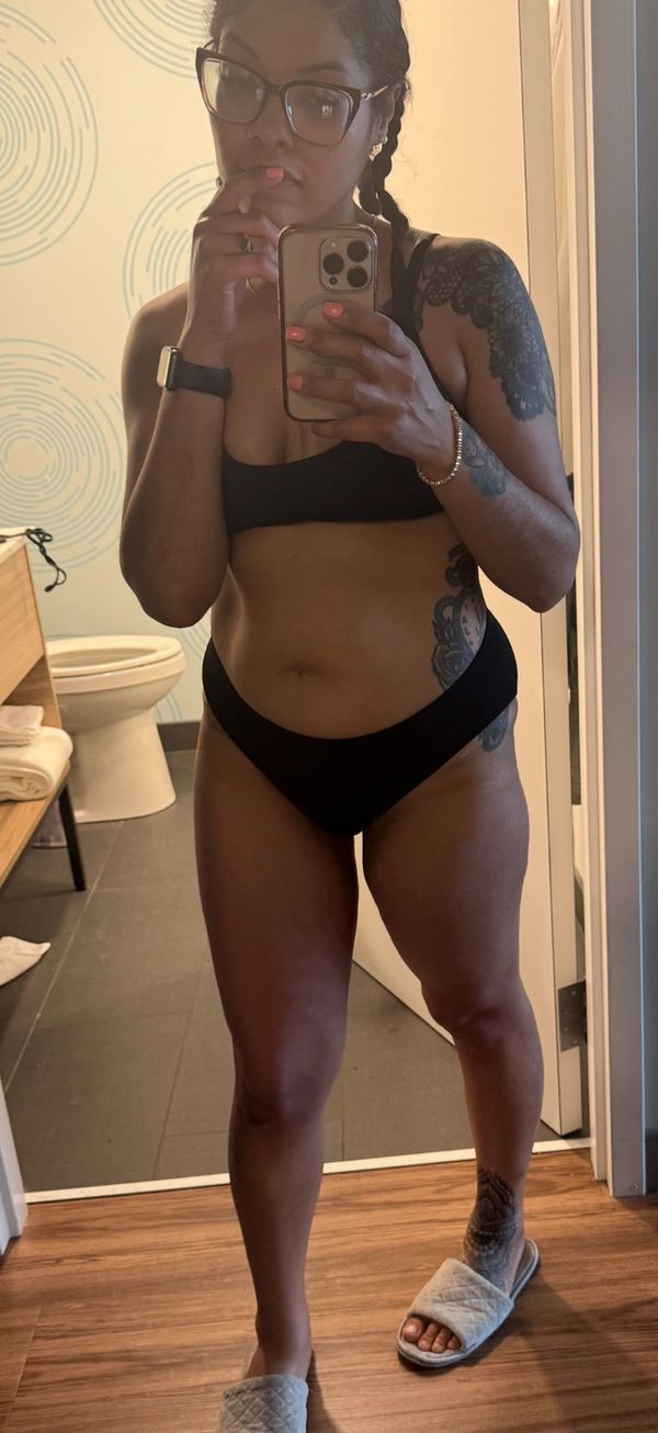 Woman in black underwear and slippers taking a mirror selfie in a bathroom.