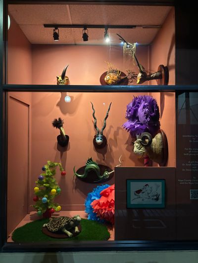 A display window with colorful masks and a decorative small tree under warm lighting.