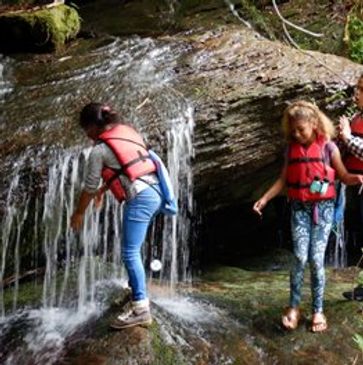 Jocassee Wild children wearing life jackets playing by a small waterfall in a forest.