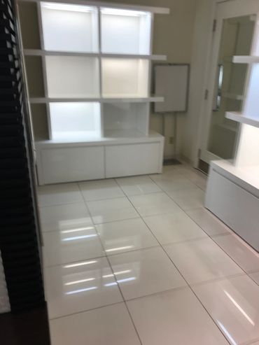 Empty white shelves and cabinets in a corner room with tiled floor.