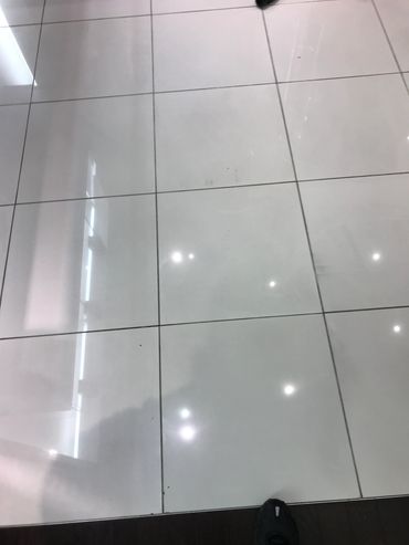 Shiny white tiled floor with reflections and a partial shoe.