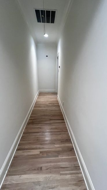 Empty narrow hallway with wooden floor and white walls.