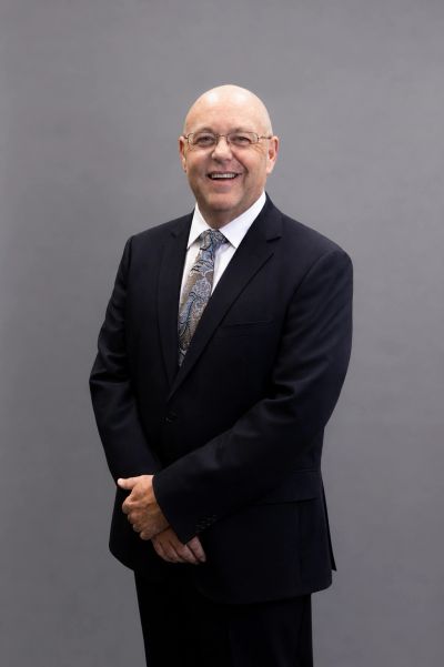 Smiling man in a suit with glasses against a gray background.