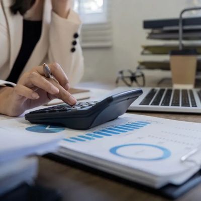 Person using a calculator with financial charts and laptop on desk.