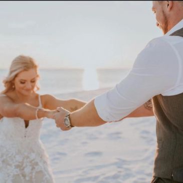 Couple holding hands on a beach at sunset.