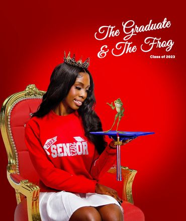 A smiling graduate with a crown holding a graduation cap with a cartoon frog on it.