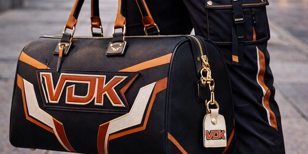 Stylish black and orange VDK leather duffle bag held by a person in matching outfit.