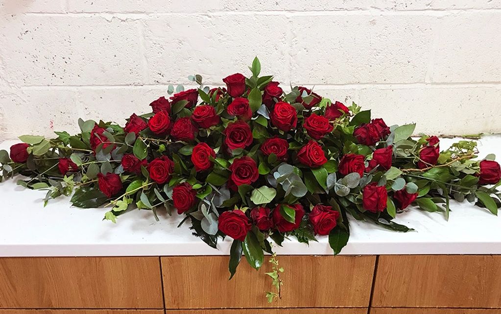 A lovely red rose coffin spray.  Beautiful, large headed roses are used together with luxury foliage