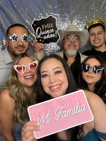 Happy family celebrating a quinceañera with festive signs and fun glasses.