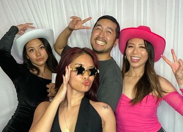 Four friends posing playfully with hats and fun expressions against a white backdrop.