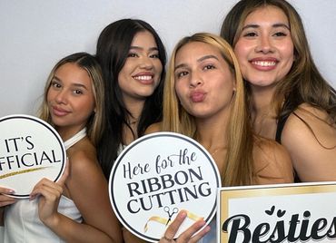 Four smiling women holding celebratory signs at a ribbon-cutting event.