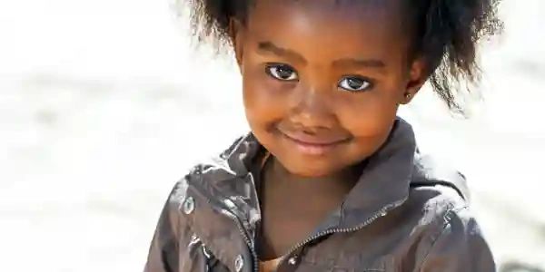 Smiling young girl with curly hair and a gray jacket.