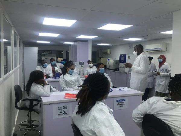 Medical professionals in a lab attending a lecture, all wearing masks and lab coats.
