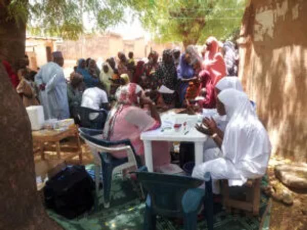 Community health workers conducting a medical check-up outdoors.
