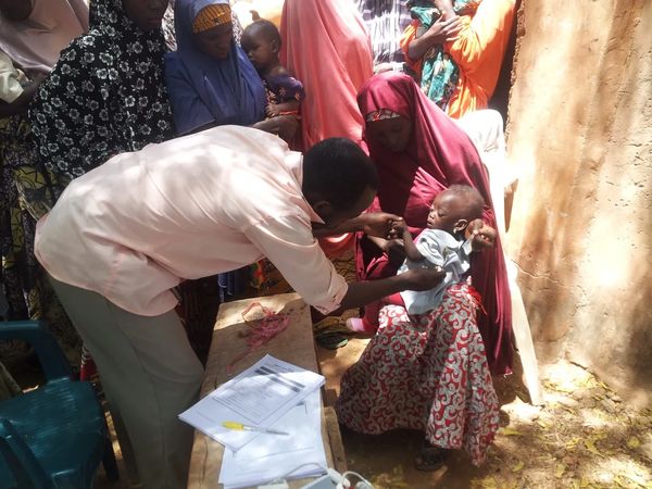 A healthcare worker examines a malnourished child held by a woman.