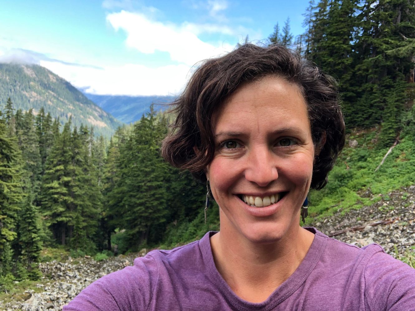 40ish single divorced white woman, short hair, wearing a purple shirt, smiling on a mountain trail.