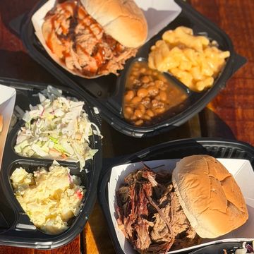 Two BBQ pulled pork sandwiches with classic sides in black trays.
