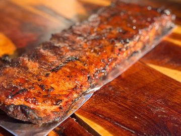 Grilled rack of ribs with a smoky, caramelized crust on a wooden board.
